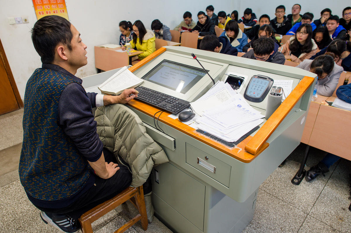 　　3月11日，湖北省武汉市，武汉大学英文系老师余功茂给大一新生上课，课堂上，余功茂声音洪亮，幽默风趣，爱与学生互动。但疾病带来的体力难支，有时让他只能跪在椅子上继续讲课。