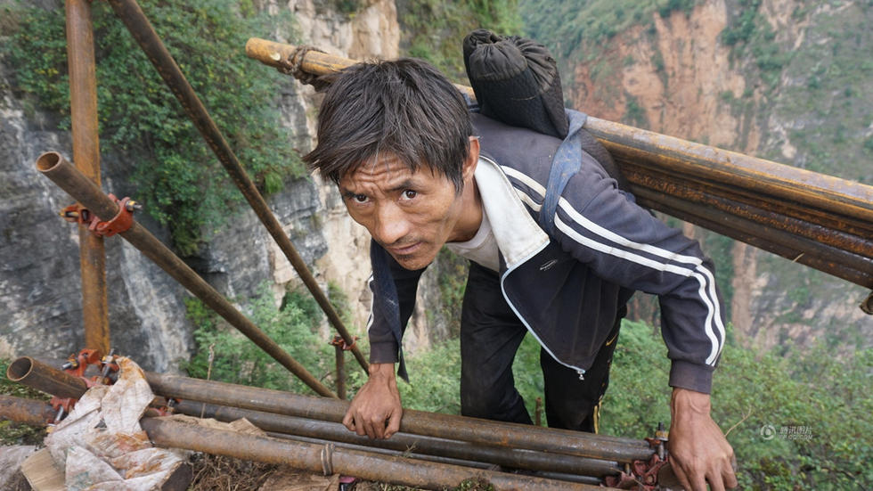 45岁的村民某色伍哈背钢管上山，钢梯将近垂直，某色伍哈紧紧抓住钢管。