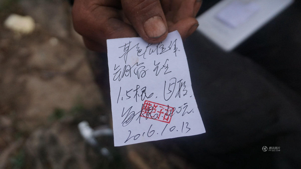 在学校门口，堆积了一捆捆钢管，每天早晨都有村民将6米长的钢管锯开，村文书莫色子古坐在一块石头上，等待前来背钢管上山修路的村民。每背走一捆，他就用一张小纸条写上背走的数量，盖上有他个人的印章，村民通过纸条结账。