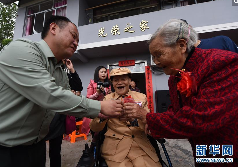 　　1950年，何光英和古臣坤定下亲事，还没举办婚礼，古臣坤就参加了志愿军，赶赴朝鲜战场。在战场上，古臣坤不幸负伤，下半身瘫痪。何光英不离不弃，在家乡悉心照顾古臣坤60多年。古臣坤老人一直有个愿望为老伴何光英补办一个婚礼。如今在当地政府、亲朋好友以及社会团体的帮助下，两位老人终于走上了红毯，完成了他们多年来的心愿。图为10月25日，前来参加婚礼的宾客向新郎古臣坤和新娘何光英送上祝福。