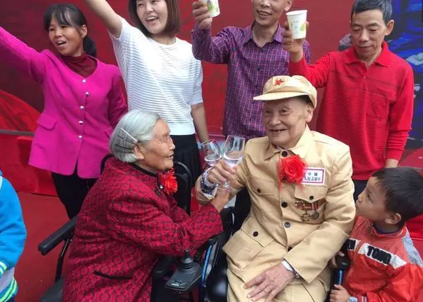 　　村口不远处，一栋两层小楼，便是81岁的何光英和老伴古臣坤的家。清晨薄雾笼罩，何光英换上红衣裳，跟往常一样，她照顾老伴如厕、穿衣，这一趟忙活下来，用了1个小时。轮椅上的古臣坤，如今83岁，白发苍苍的老人换上了崭新的军装，他小心翼翼地拿出珍藏已久的黄色盒子，打算佩戴上保存了一生的4枚荣誉胸章，迎接这场最为重要的仪式。