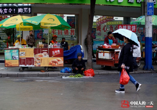 　　凄风冷雨中，老人穿过几条街后，将青菜摆在早点的摊位旁边，等候市民光顾。